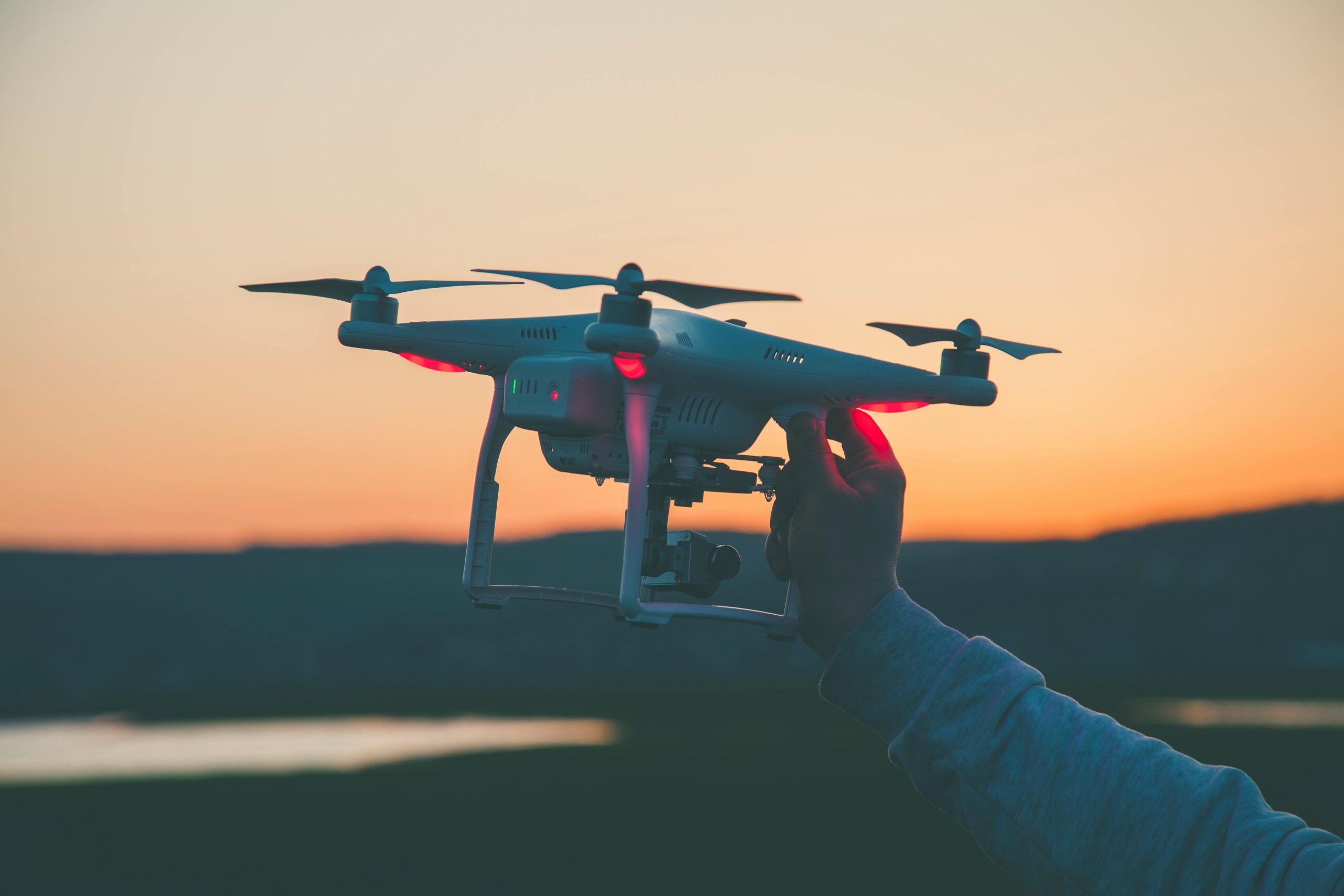 Silhouette of a drone and hand against a colorful sunset backdrop.